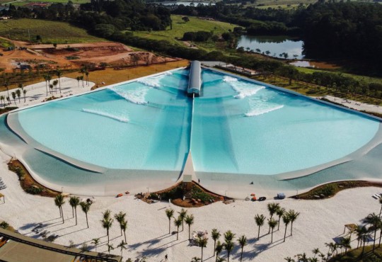 Além da piscina com ondas, o espaço ainda inclui uma longa faixa de areia e paisagismo litorâneo