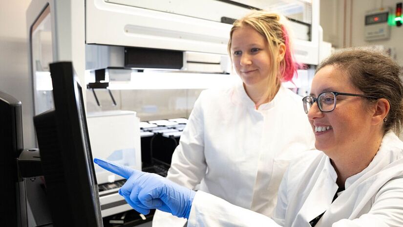 A cientista Ana Rita Brochado e Laura Sniegula analisam dados do robô de pipetagem; estudo mostra que a cafeína altera proteínas de transporte na E. coli/ Leon Kokkoliadis/CMFI/Universidade de Tübingen