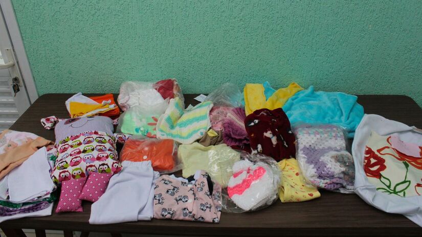 O enxoval conta com 3 pagãos, 2 macacões, 2 casacos, 2 toucas de lã, 2 sapatinhos de lã, 2 fraldas de tecido, 2 panos de boca, manta, cobertor, bolsa artesanal e 'naninha do bem' / Júlia Morgado/Diário do Litoral