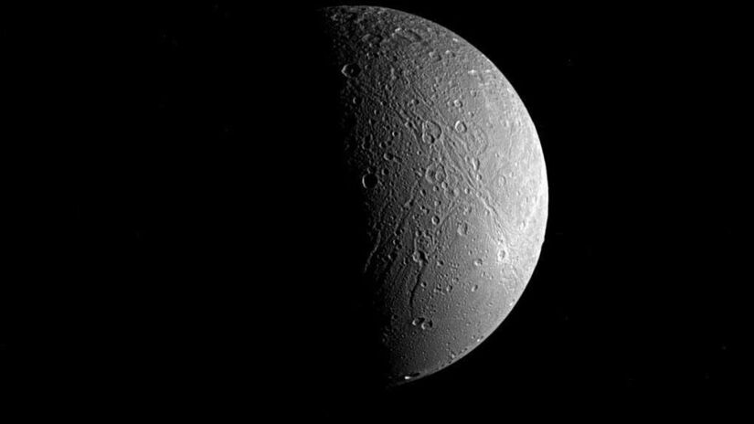 Dione: Composta principalmente de gelo, Dione apresenta grandes penhascos gelados e marcas brilhantes, sugerindo intensa atividade geológica no passado - NASA