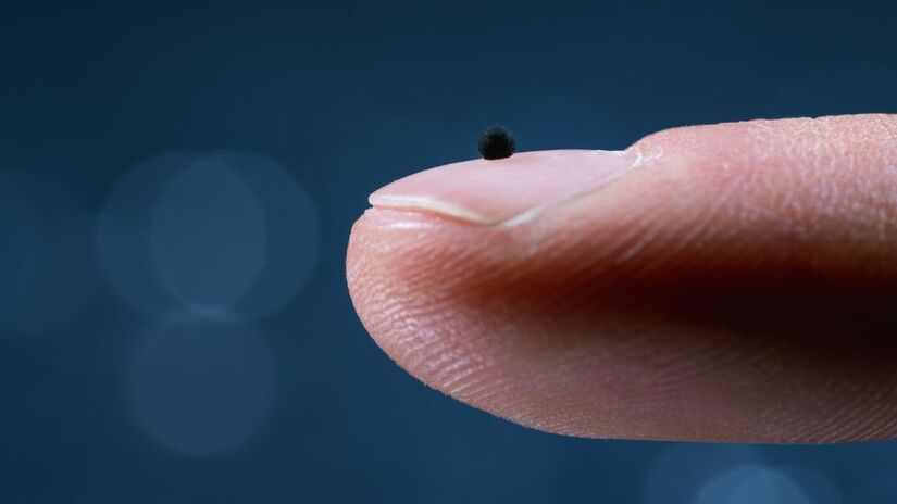 O microrrobô em escala real, visto sobre a ponta do dedo, destaca sua dimensão minúscula e capacidade de operar em vasos extremamente estreitos/ Luca Donati/ETH Zürich