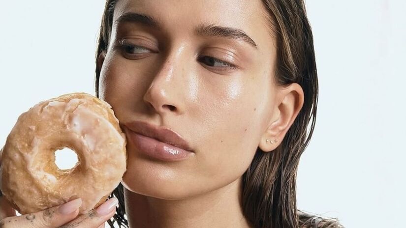 Popularizada por Hailey Bieber, a tendência glazed donut skin propõe uma pele iluminada e hidratada, com brilho cristalino que lembra o glacê de uma rosquinha. O visual valoriza menos maquiagem e mais cuidados diários, reforçando a importância da limpeza, hidratação e proteção solar/ Reprodução Instagram/@haileybieber