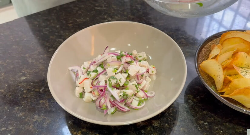 Corte a tilápia em cubos do tamanho desejado e transfira para um recipiente. Adicione o suco de limão, a cebola, a pimenta, o alho e o gengibre. Reprodução/Youtube/Julia Nakaya