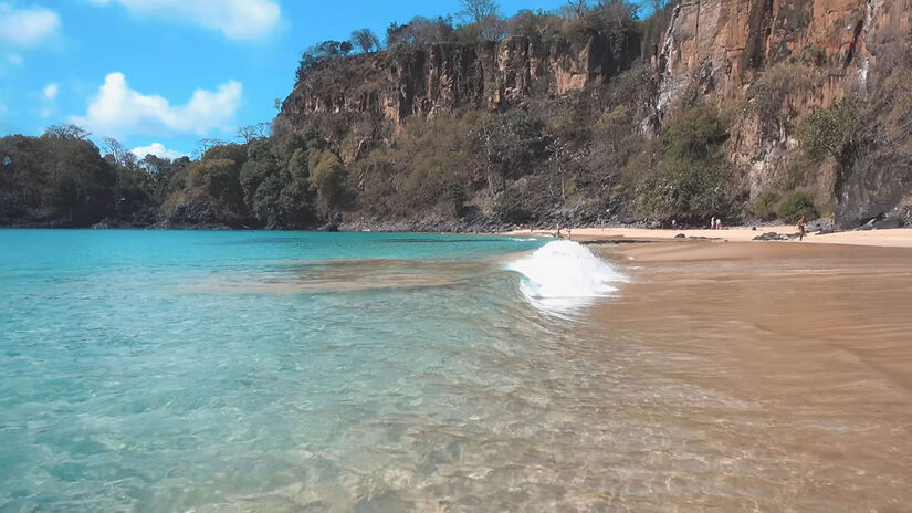 Do alto do paredão, a vista panorâmica revela o contraste entre o azul-turquesa e a vegetação nativa preservada / Foto: Reprodução/YouTube Viagens Cine