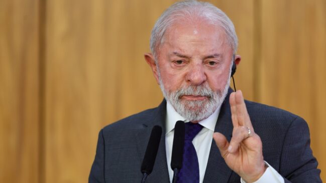 Homem de terno falando ao microfone e fazendo gesto com a mão durante discurso.