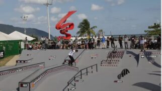 Skatista realizando manobra em pista de street durante competição, com público ao redor e escultura vermelha ao fundo.