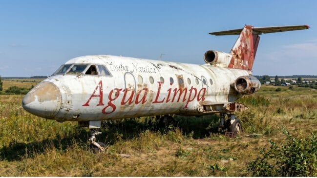 Avião abandonado e enferrujado em área rural, com a inscrição “Água Limpa” na fuselagem.