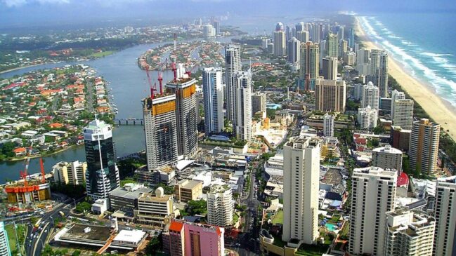 Vista aérea de Gold Coast, na Austrália, com prédios altos próximos à praia, canal com casas ao redor e faixa extensa de areia ao lado do mar