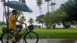Homem de bicicleta e guarda-chuva pedala na orla da praia de Santos