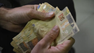 A imagem mostra uma pessoa contando dinheiro em espécie