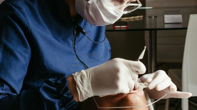 Dentista realiza procedimento na boca de paciente deitado na maca