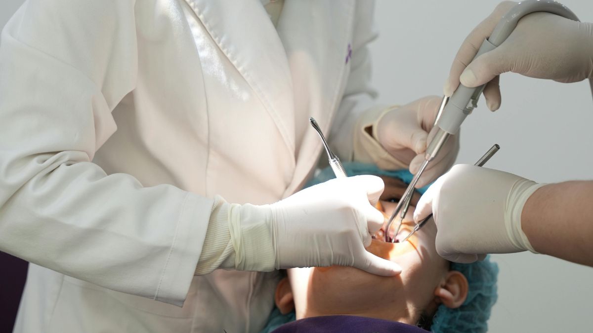 Dentista realiza procedimento com instrumentos odontológicos em paciente deitado na cadeira