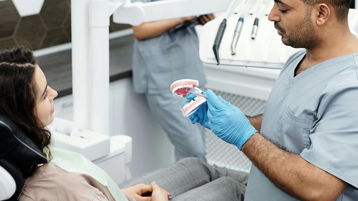 Dentista explica tratamento usando modelo de dentes para paciente em consultório odontológico