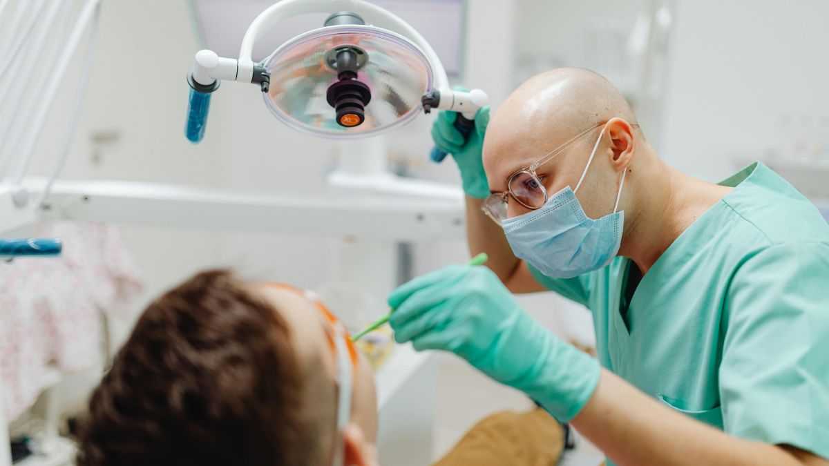 Dentista com máscara e luvas examina paciente durante atendimento clínico odontológico