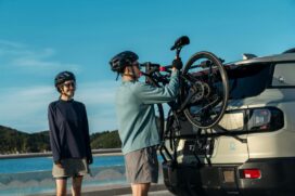 Enquanto mulher observa, homem coloca bicicleta em suporte para transportar bike na traseira do carro.