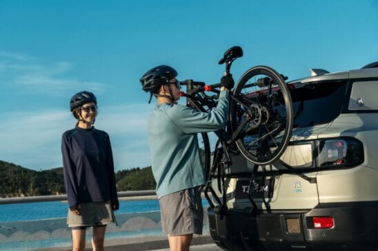 Enquanto mulher observa, homem coloca bicicleta em suporte para transportar bike na traseira do carro.