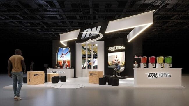 Estande da Optimum Nutrition em feira fitness, com estrutura moderna em preto e branco, iluminação geométrica, balcão com bebidas coloridas e espaços interativos para visitantes.