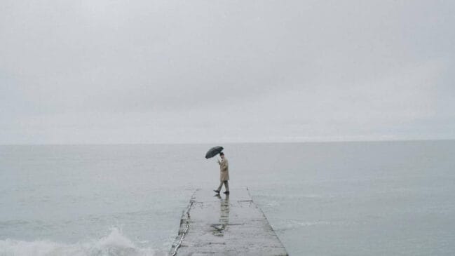 Homem curte a chuva, o frio e o dia cinza na beira do mar