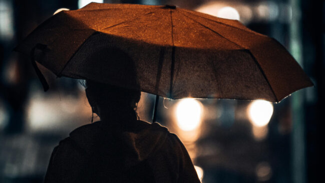 A imagem mostra uma mulher caminhando a noite