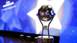 Troféu oficial de prata da Copa Sul-Americana em destaque contra um painel digital iluminado em tons de azul