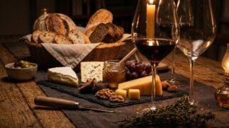 Mesa de jantar de madeira decorada à luz de velas com petiscos gourmet, queijos finos e vinho para degustação
