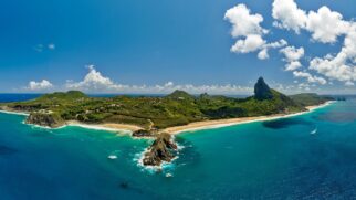 Vista aérea panorâmica de Fernando de Noronha, destacando o Morro do Pico e praias de areia clara cercadas por mar verde-turquesa