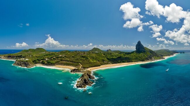 Vista aérea panorâmica de Fernando de Noronha, destacando o Morro do Pico e praias de areia clara cercadas por mar verde-turquesa