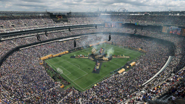 Visão panorâmica do MetLife Stadium lotado durante uma cerimônia no gramado. O campo de futebol apresenta uma estrutura circular central com fumaça e bandeiras coloridas, onde se lê "One Dream, One Champion". As arquibancadas estão repletas de espectadores sob um céu nublado, e telões exibem informações do evento. No horizonte, é possível ver o skyline de uma cidade.