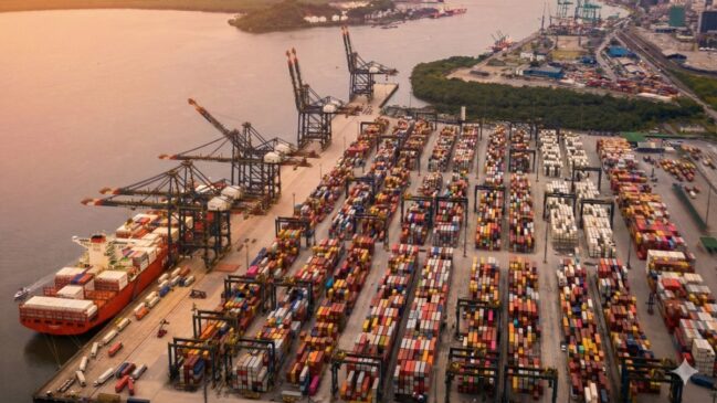 Vista aérea de um terminal portuário com milhares de contêineres coloridos organizados em fileiras e grandes guindastes de carga