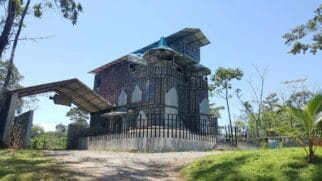 Estrutura arquitetônica contemporânea à beira-mar sob céu nublado, com ondas colidindo contra as pedras ao fundo.