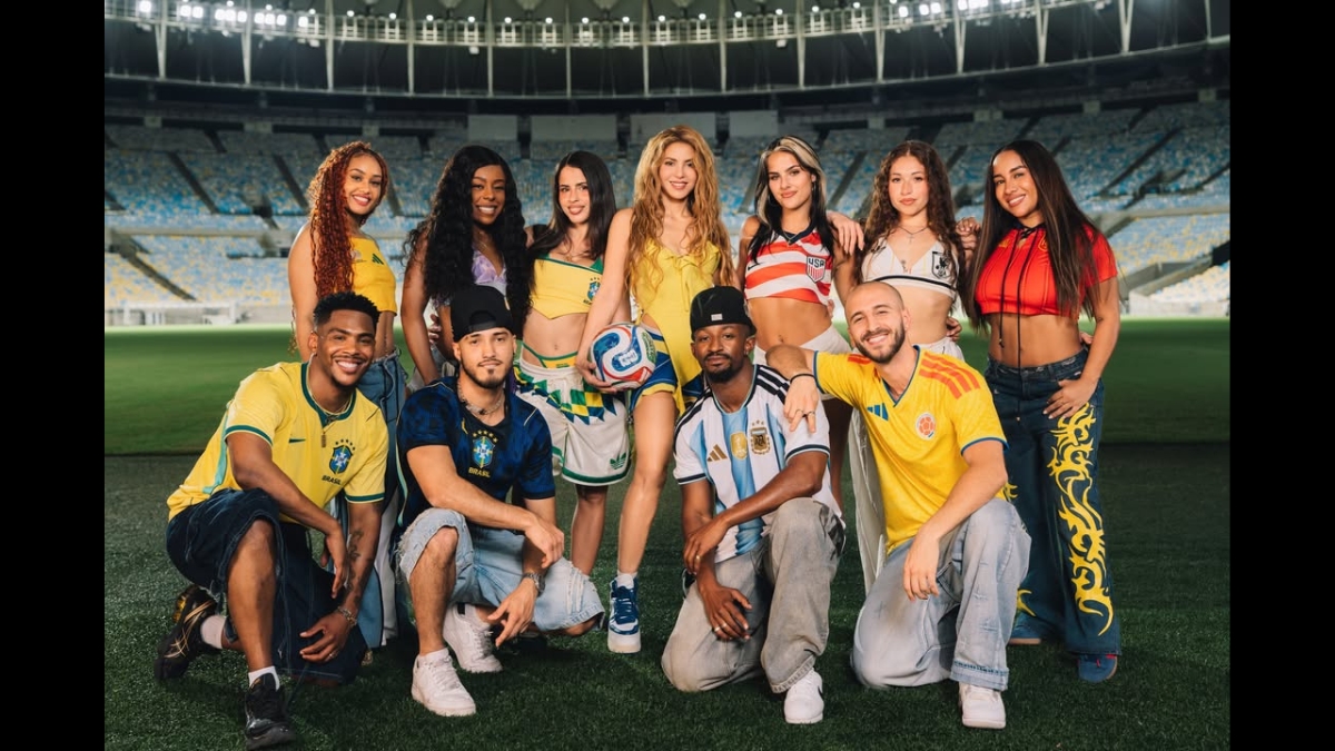 Foto promocional de Shakira no centro, cercada por um grupo diversificado de dançarinos e artistas, todos usando roupas com as cores de várias bandeiras nacionais, em um estádio de futebol vazio.