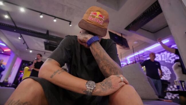 Neymar Jr. chorando, curvado para frente com a mão no rosto, usando um boné marrom da Red Bull.