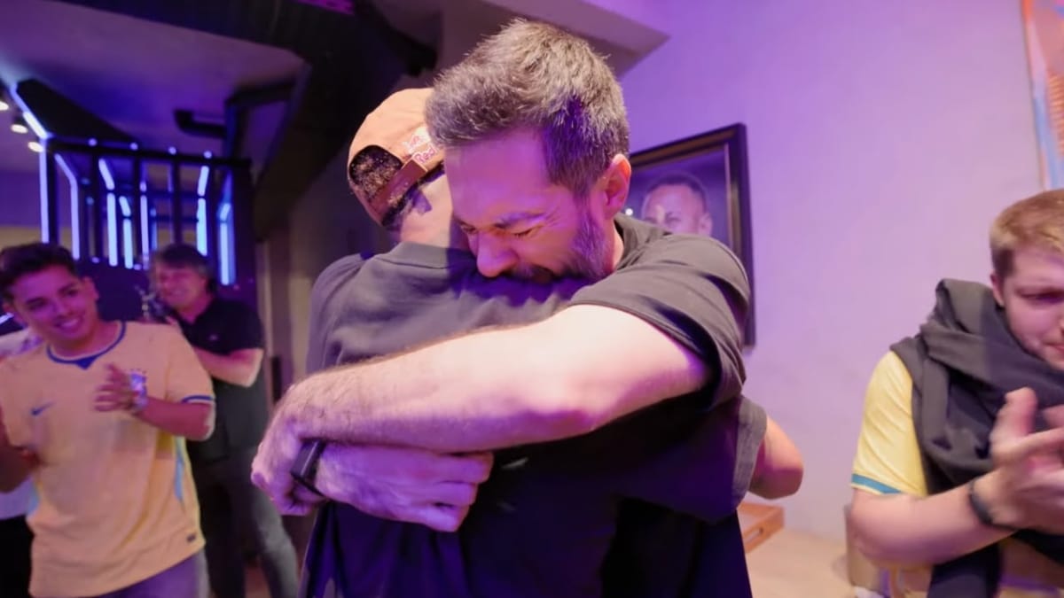 Neymar Jr. dando um abraço forte em um homem de barba, enquanto pessoas ao fundo aplaudem.