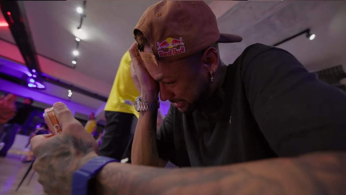 Neymar Jr. emocionado, cobrindo o rosto com a mão enquanto segura o celular em uma videochamada com um homem mais velho.