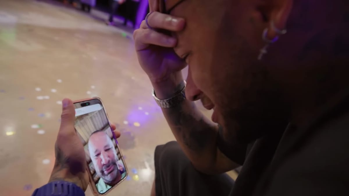 Neymar Jr. emocionado, cobrindo o rosto com a mão enquanto segura o celular em uma videochamada com um homem mais velho.