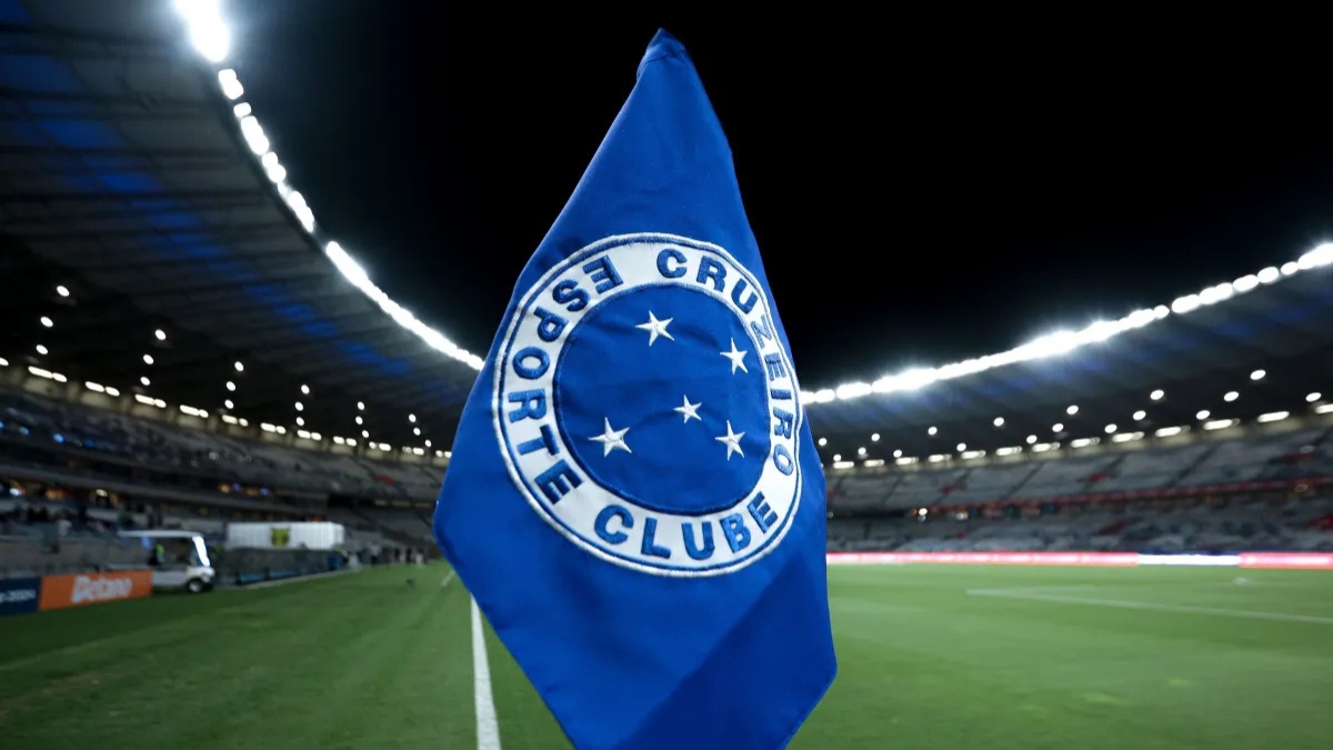 Bandeira do Cruzeiro posicionada no gramado de um estádio iluminado.