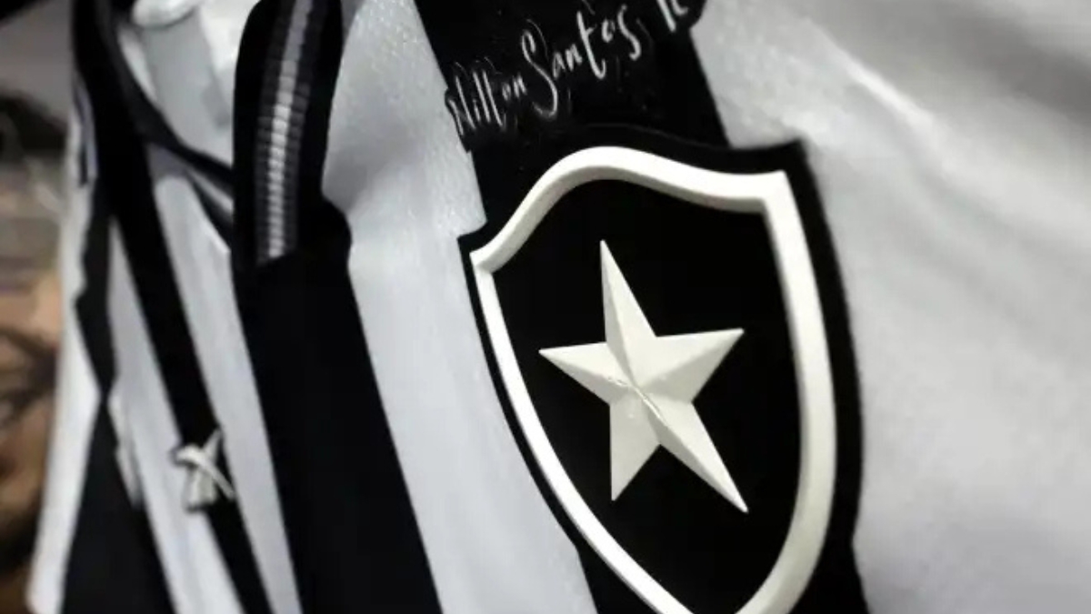 Close-up do escudo do Botafogo, a Estrela Solitária branca sobre fundo preto, fixado em uma camisa de futebol listrada em preto e branco.