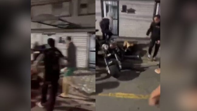 A imagem apresenta dois quadros capturados de vídeos de celular que registram o momento da confusão nas ruas próximas ao local do evento. No lado esquerdo, observa-se um grupo de jovens em movimento caótico, com algumas pessoas vestindo roupas escuras e outras com bermudas claras, sugerindo uma correria generalizada em frente a uma estrutura que parece ser a entrada de uma garagem ou prédio. Já no quadro da direita, a cena foca em uma motocicleta estacionada na calçada, enquanto indivíduos ao redor aparecem em atitudes de confronto ou observação da briga. A qualidade das capturas é típica de gravações amadoras feitas à noite, com baixa luminosidade e desfoque de movimento, o que reforça o clima de tensão e a rapidez com que os fatos ocorreram durante a mobilização policial mencionada.