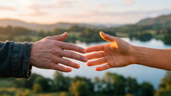 Duas mãos se aproximando sob uma luz suave, simbolizando a superação do ódio através do amor no Budismo e no Cristianismo