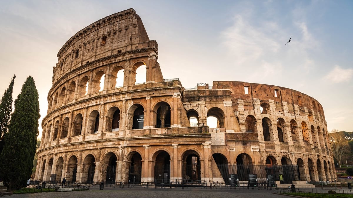 Vista do Coliseu de Roma em destaque durante o entardecer, com céu claro ao fundo