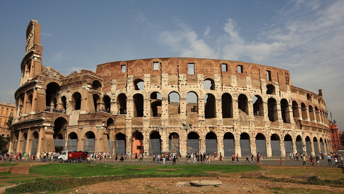 Turistas caminham em frente ao Coliseu de Roma em dia ensolarado