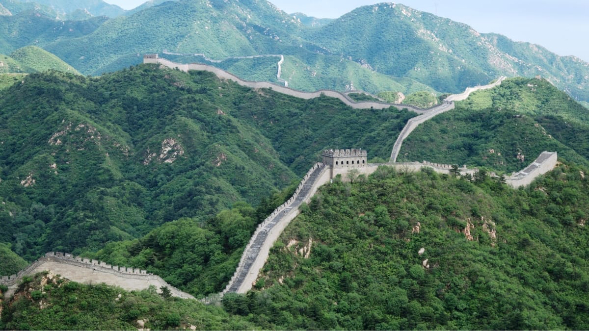 Trecho da Grande Muralha da China atravessa montanhas cobertas por vegetação verde