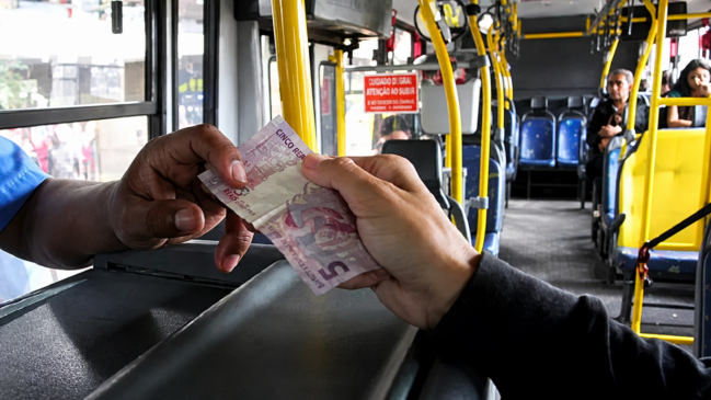 Passageiro paga passagem de ônibus em dinheiro com uma nota de R$ 5