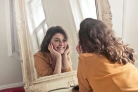 Fotografia em plano médio de uma mulher sorridente com camisa jeans olhando diretamente para a câmera contra um fundo claro