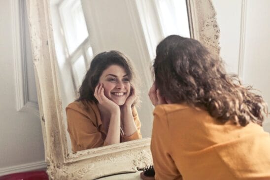 Fotografia em plano médio de uma mulher sorridente com camisa jeans olhando diretamente para a câmera contra um fundo claro