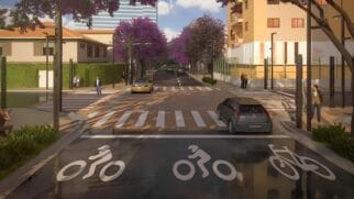 A imagem apresenta uma projeção arquitetônica tridimensional (renderização) que ilustra o projeto de reurbanização de uma via urbana, com foco em acessibilidade, paisagismo moderno e organização do trânsito. A cena é retratada a partir de uma perspectiva central, ao nível da rua. Primeiro Plano e Ciclovia Na parte inferior da imagem, em primeiro plano, destaca-se um trecho de ciclovia com pavimento asfáltico escuro e liso. Três grandes pictogramas brancos pintados no chão indicam a exclusividade para ciclistas: os dois primeiros mostram silhuetas estilizadas de pessoas pedalando e o terceiro exibe apenas o desenho de uma bicicleta. Uma linha branca contínua delimita o fim dessa faixa. O Cruzamento e os Veículos Logo após a ciclovia, há um cruzamento viário estruturado com faixas de pedestres sinalizadas em branco. O piso do cruzamento apresenta uma tonalidade marrom-clara, sugerindo o uso de blocos intertravados de concreto (pavers). Dois carros estão inseridos na via: À direita: Um veículo moderno do modelo hatchback, na cor cinza-escura, está posicionado de costas, avançando em direção ao cruzamento. Ao centro: Um carro de passeio na cor amarela ou dourada trafega no sentido oposto, mais ao fundo da via principal. Pedestres e Infraestrutura Urbana Diversas figuras humanas estilizadas estão distribuídas pelas calçadas para simular o uso do espaço público: No canto inferior esquerdo, um homem agachado parece registrar a cena. Próximo à faixa de pedestres da esquerda, um homem de terno caminha em direção à via, enquanto um casal conversa mais ao fundo, perto de uma cerca viva alta e verde. Na calçada da direita, um pedestre caminha em primeiro plano e, mais atrás, um casal anda abraçado perto de um edifício residencial de cor amarela-clara com varandas. Postes de iluminação pública modernos, esguios e na cor preta estão posicionados estrategicamente ao longo das calçadas em ambos os lados da rua. Nota-se a total ausência de fiação aérea. Paisagismo e Elementos ao Fundo O projeto paisagístico é um dos grandes destaques da imagem. Árvores de médio porte com copas densas e repletas de flores na cor roxa ou jambo (características de ipês) margeiam os dois lados da avenida, estendendo-se em direção ao fundo da perspectiva. Canteiros com vegetação rasteira verde decoram as esquinas em primeiro plano. Ao fundo, a rua continua em linha reta com mais veículos distantes, sob um céu azul-claro com nuvens brancas esparsas. No horizonte, ergue-se a silhueta de um edifício comercial alto e moderno com fachada espelhada em tons azulados.