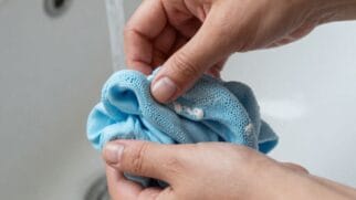 Mãos úmidas seguram uma esponja azul, que está suja de detergente