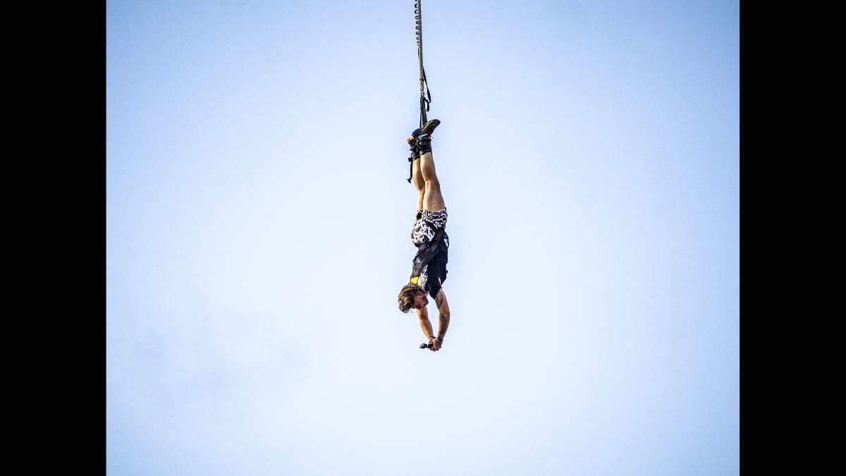 Atleta salta de penhasco utilizando equipamento de base jump.