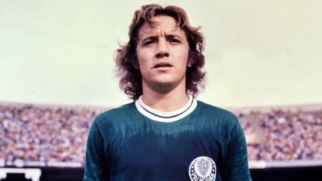 Retrato em meio-corpo de atleta com uniforme antigo do Palmeiras à frente de uma arquibancada lotada de estádio