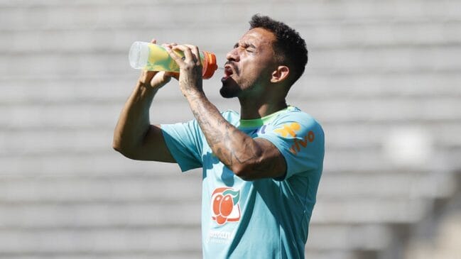 A imagem mostra o jogador Danilo, do Flamengo e da Seleção Brasileira, durante um treinamento ou atividade esportiva, usando uniforme de treino e bebendo água de uma garrafa esportiva.